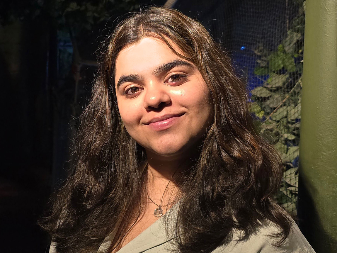 A college student with long dark hair smiles at the camera